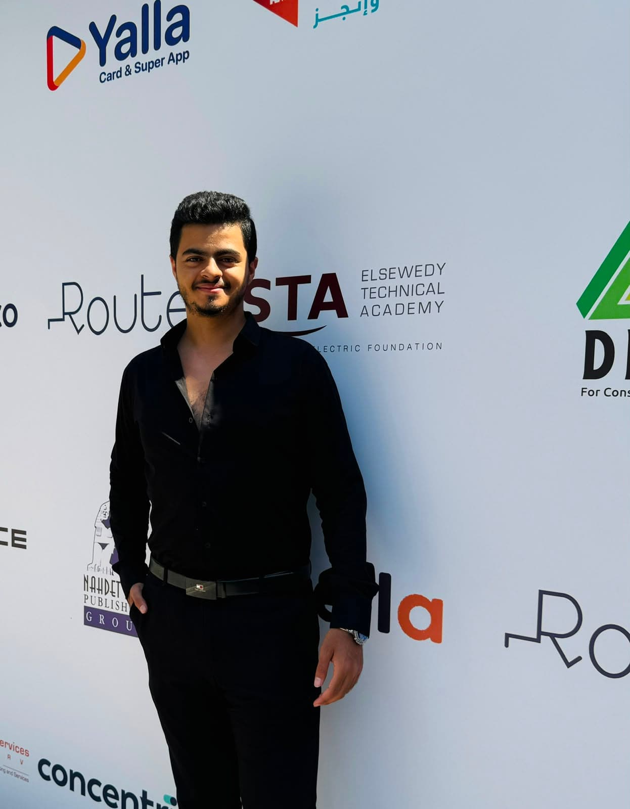Kariem Ibrahem standing in front of a sponsor wall at an industry event